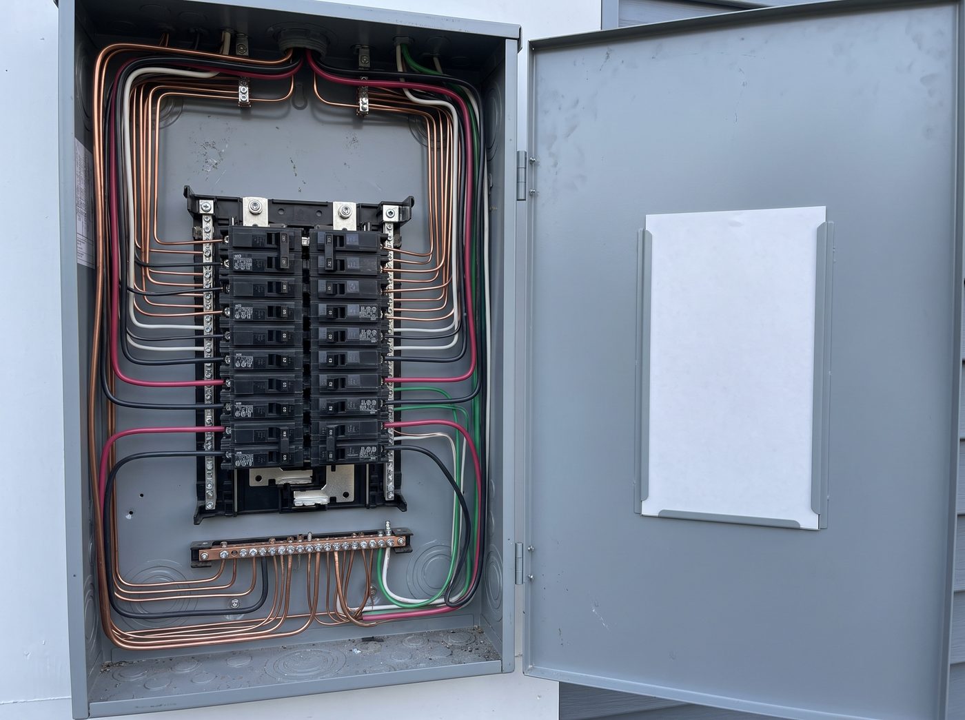 The inside of a finished residential panel with the cover off: conductors dressed in neat parallel runs with square bends, breakers seated in an even row, and a blank circuit directory card on the open door.